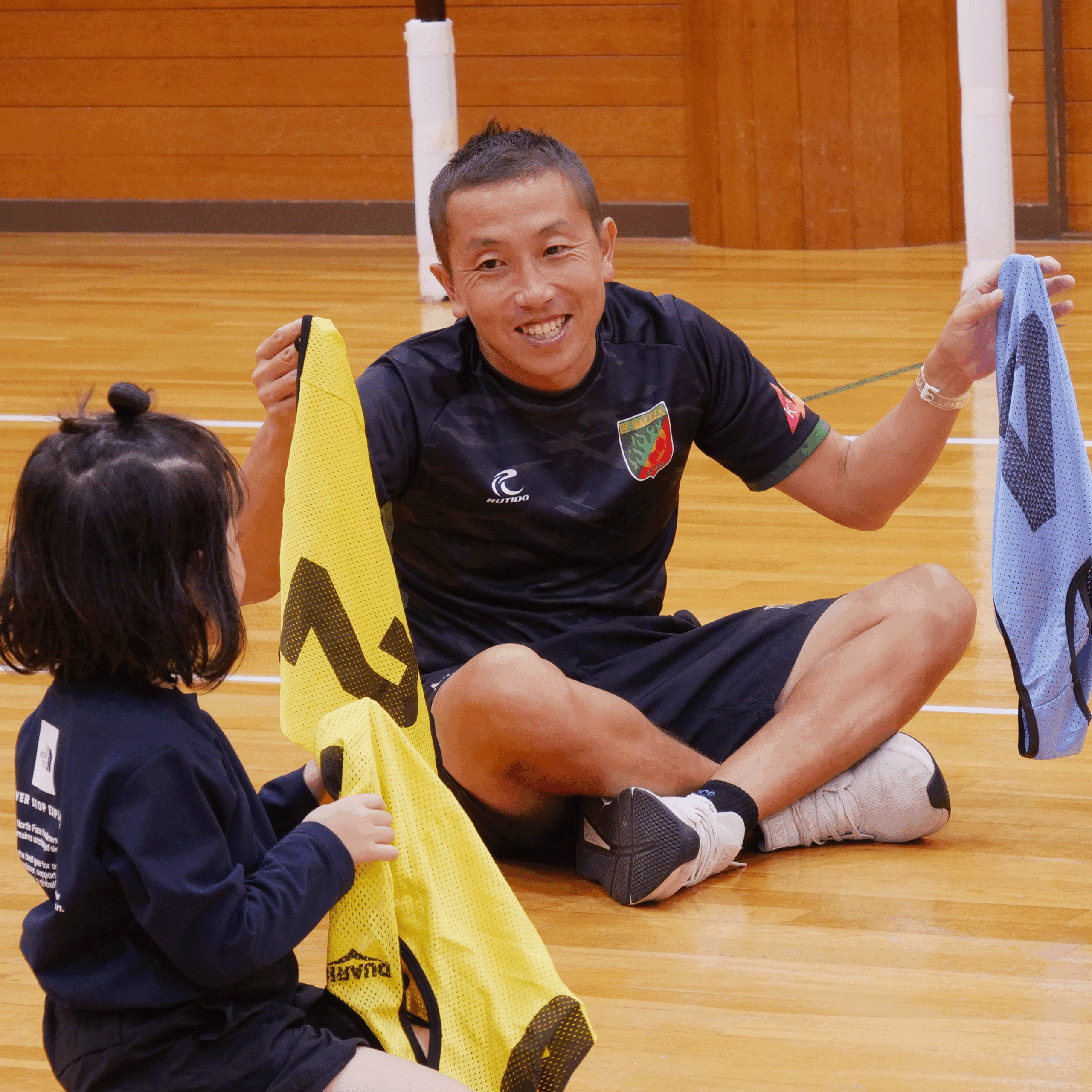 笑顔で子供たちに試合のユニフォームを渡す講師