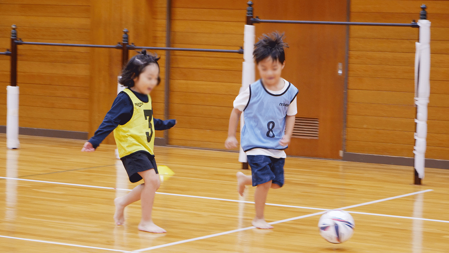 サッカーボールを追って走る子ども二人