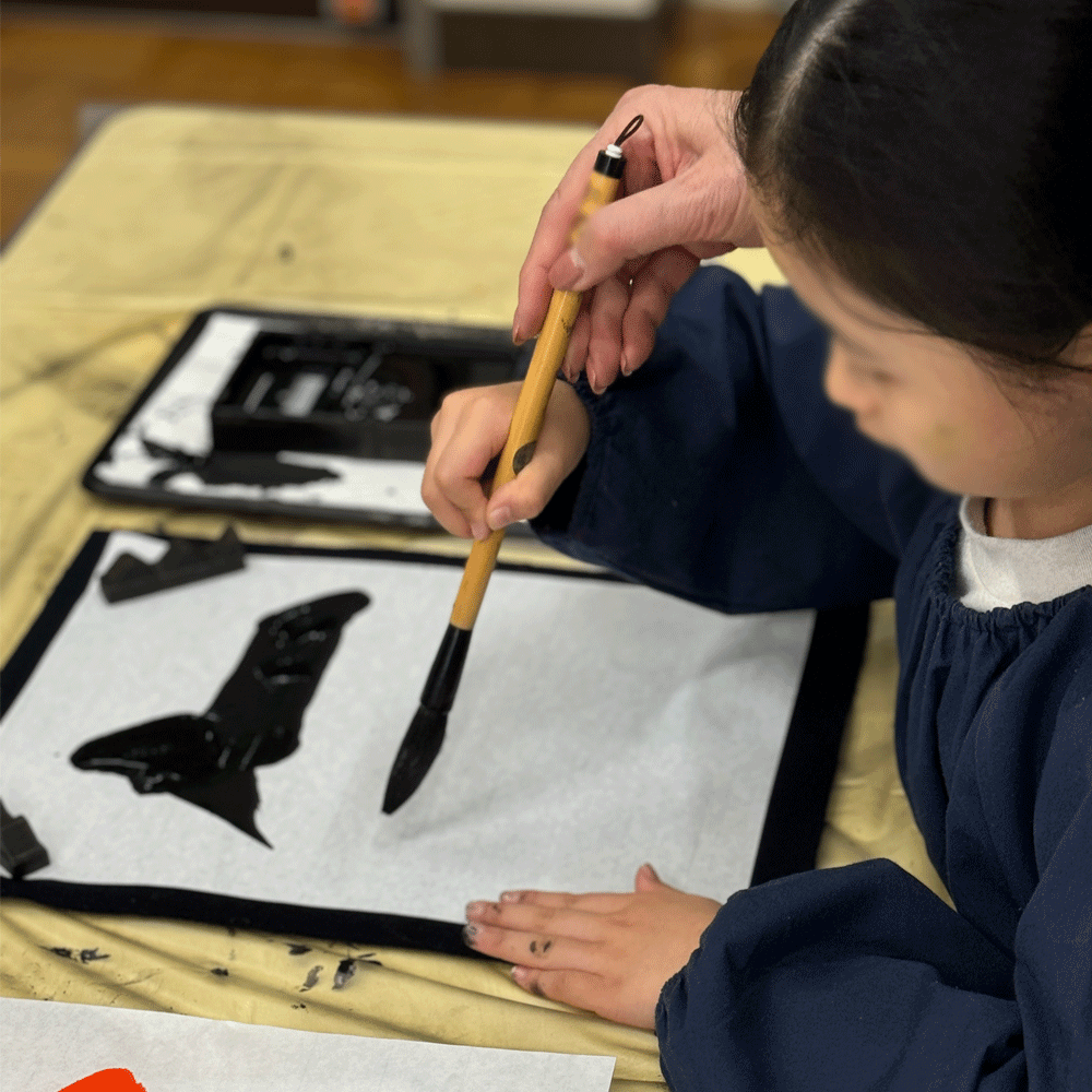 先生といっしょに筆を持って書く子ども
