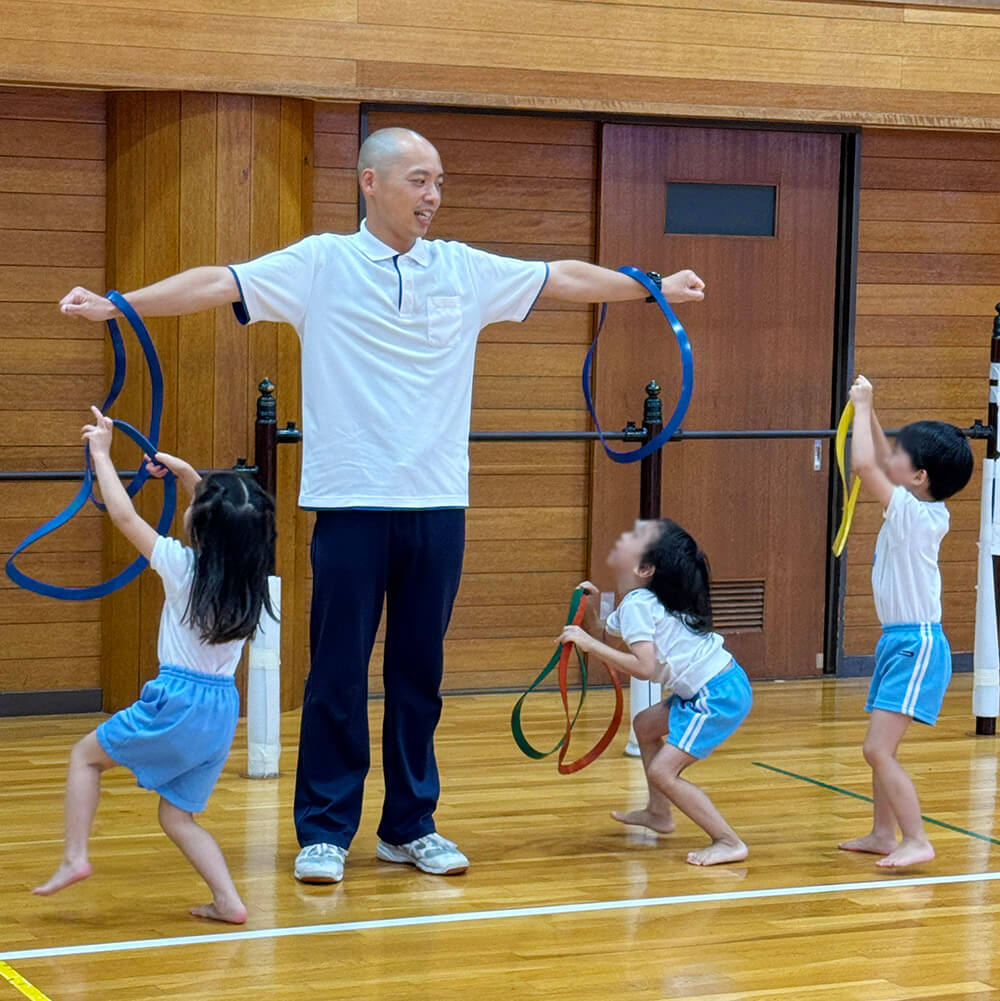 ゲームで使ったフープを講師の腕にかけてあそぶ子どもたち
