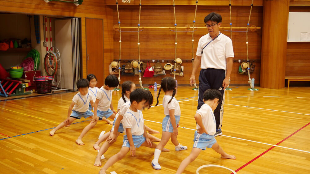 準備運動で足を開く子どもたちと確認する講師｜パドマ幼稚園体操教室