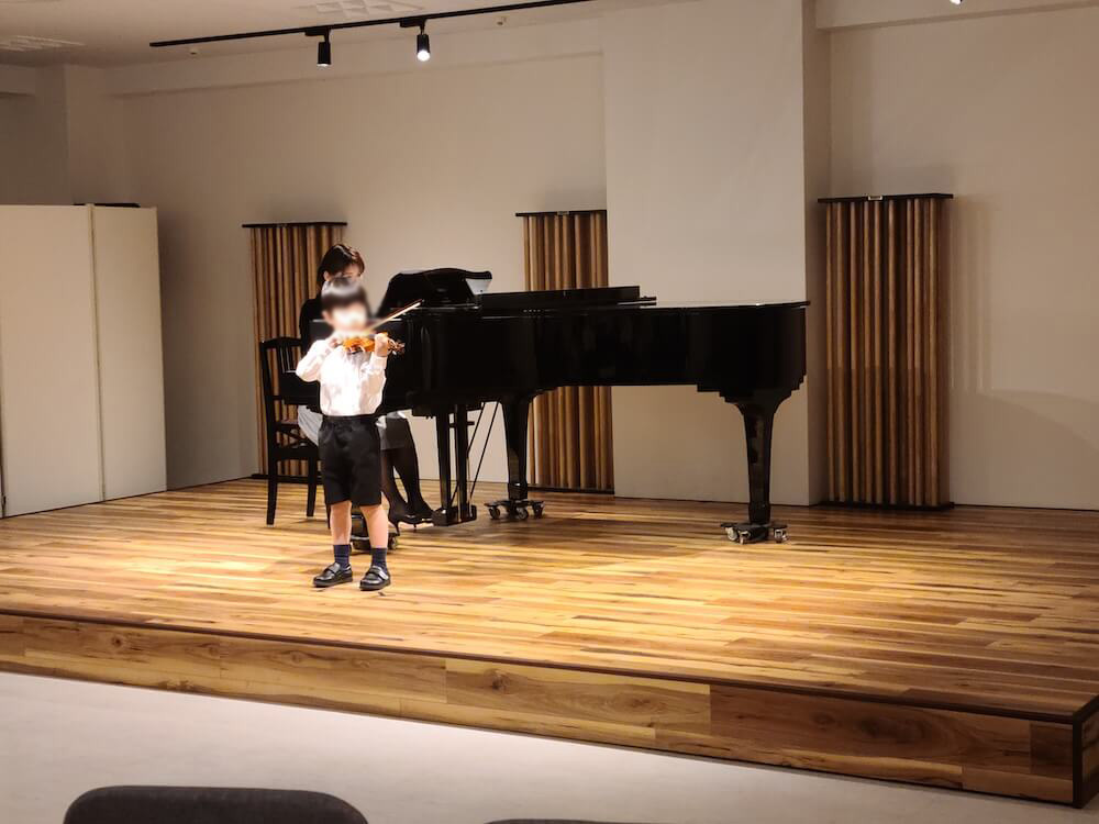 ホールの発表会でピアノ伴奏付きのソロ演奏をする子ども