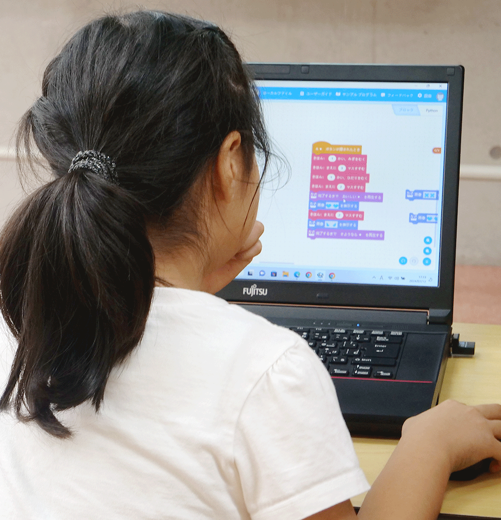 パソコンとロボットでプログラミングを学ぶ子ども